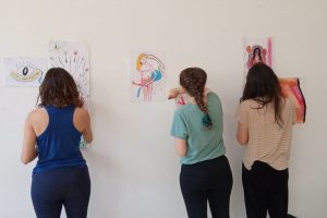 Tres mujeres haciendo trabajos de arteterapia gestalt sobre la pared.