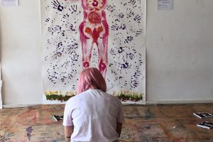 Cartografía corporal en pintura colgada de la pared con alumna de arteterapia tomando apuntes durante un Introductorio de Arteterapia Gestalt